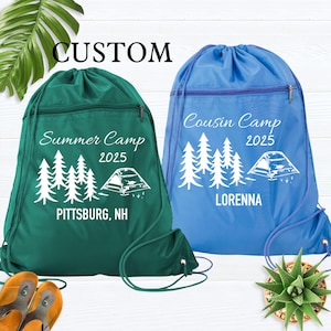 May include: Two drawstring backpacks, one green and one blue, with white text and graphics. The green bag says "Summer Camp 2025" and "Pittsburg, NH." The blue bag says "Cousin Camp 2025" and "Lorenna."