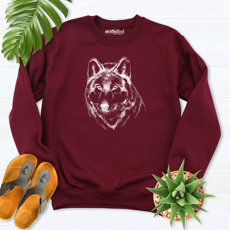 Pu&ograve; includere: Felpa color borgogna con un'illustrazione di lupo bianco sul davanti. La felpa ha un collo rotondo e maniche lunghe. Il testo "shirtthatcool" &egrave; stampato sulla parte superiore della felpa.