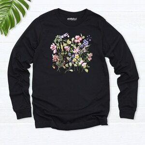 K&ouml;nnte beinhalten: Schwarzes Langarmshirt mit einem Blumendruck mit rosa, lila, gelben und wei&szlig;en Blumen. Das Shirt hat den Text "shirtatwork" auf der Vorderseite.