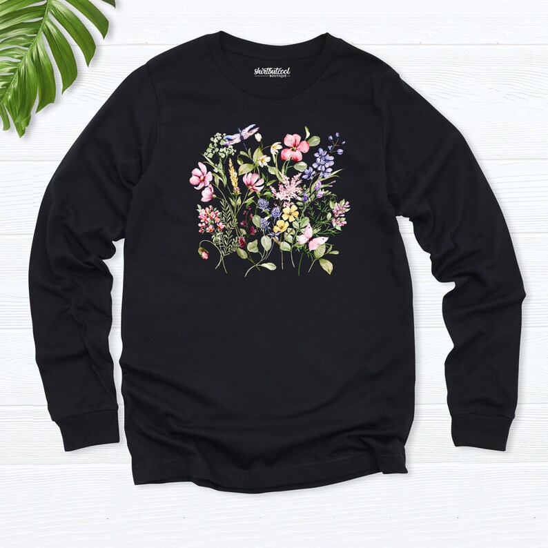K&ouml;nnte beinhalten: Schwarzes Langarmshirt mit einem Blumendruck mit rosa, lila, gelben und wei&szlig;en Blumen. Das Shirt hat den Text "shirtatwork" auf der Vorderseite.