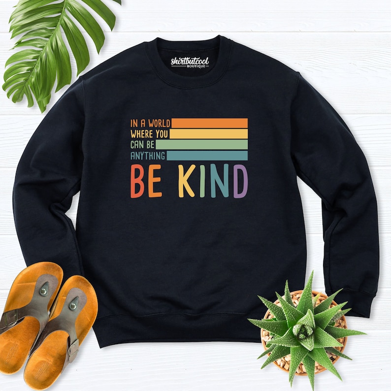 May include: Black sweatshirt with a rainbow stripe design and the text "In a world where you can be anything be kind".
