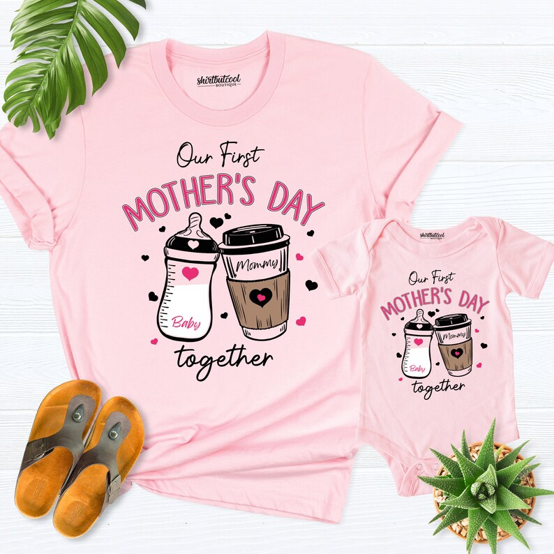 May include: Pink t-shirt and onesie set featuring a graphic of a baby bottle and a coffee cup. The text reads "Our First Mother's Day Together".