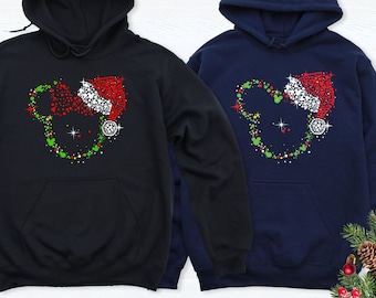 Puede incluir: Dos sudaderas con capucha, una negra y otra azul marino, cada una con un gráfico de una silueta con forma de ratón delineada con puntos rojos, verdes y blancos. El diseño incluye un gorro de Papá Noel rojo con borde blanco.
