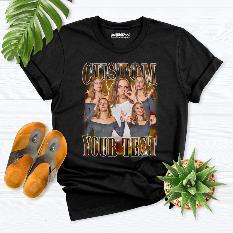May include: Black t-shirt with a custom design featuring a collage of images and the text "CUSTOM YOUR TEXT" in a retro style. The shirt is displayed with a pair of orange and brown sandals and a small potted succulent.