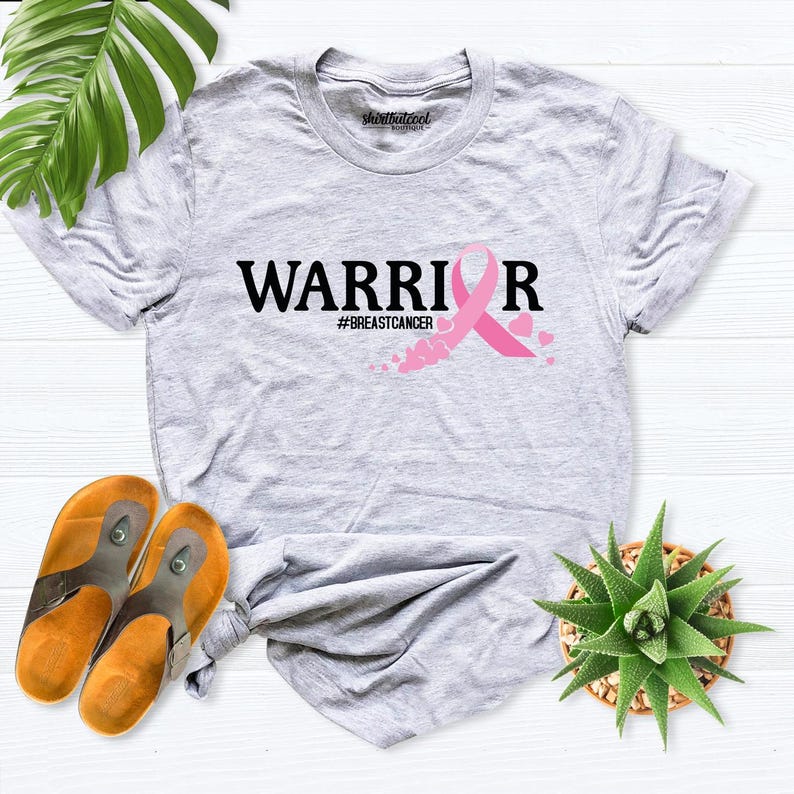 May include: Gray t-shirt with the text "WARRIOR" and a pink ribbon with the hashtag "#BREASTCANCER".