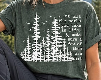Peut inclure: Un t-shirt à manches courtes vert foncé avec un motif blanc représentant une forêt de pins et des oiseaux. Le texte indique : of all the paths you take in life, make sure a few of them are dirt. Le t-shirt possède un col rond et une coupe décontractée.