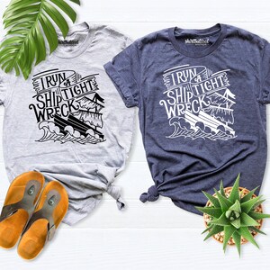 May include: Two t-shirts with a graphic of a ship and the text "I run a ship tight wreck". The t-shirt on the left is light gray and the t-shirt on the right is dark blue.