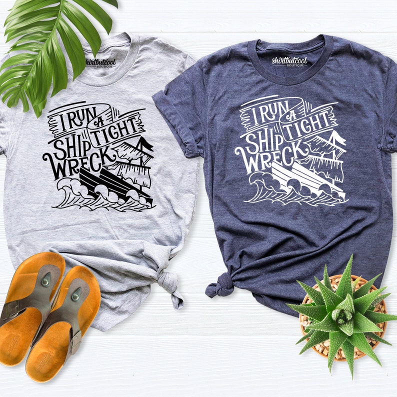 May include: Two t-shirts with a graphic of a ship and the text "I run a ship tight wreck". The t-shirt on the left is light gray and the t-shirt on the right is dark blue.