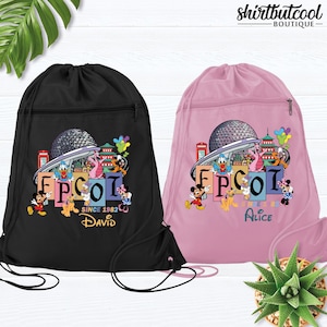 May include: Black and pink drawstring backpacks with a colorful EPCOT graphic featuring Mickey Mouse, Donald Duck, and other Disney characters. The black bag has "David" and the pink bag has "Alice" printed on it. The text "Since 1982" is also visible.
