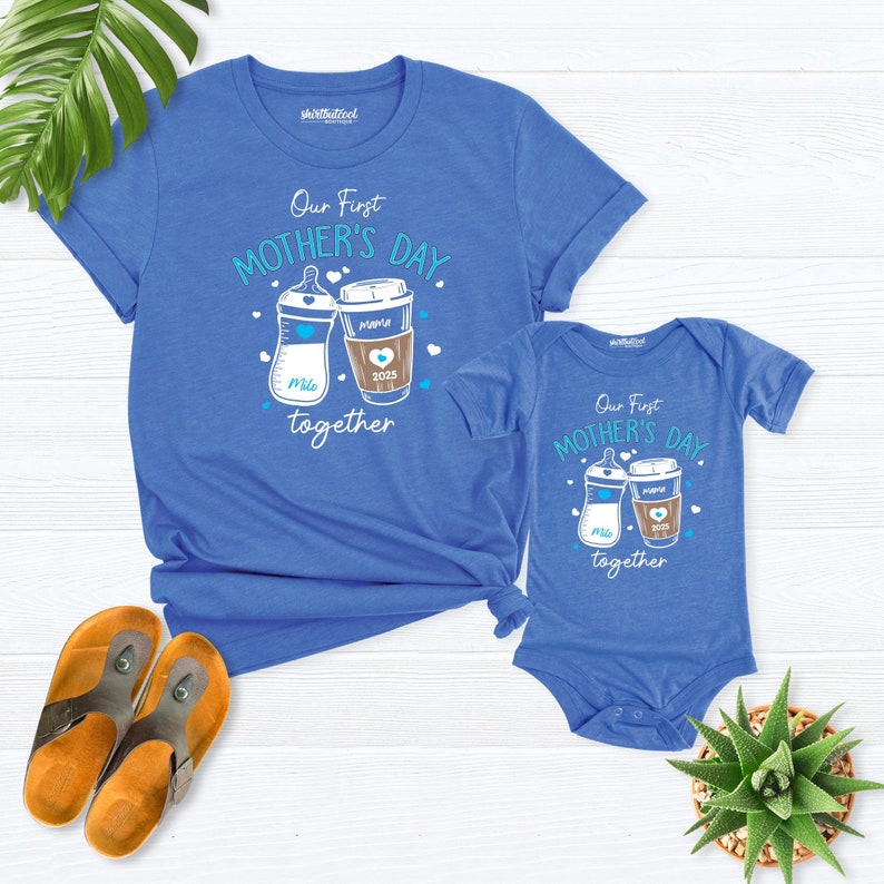 May include: Blue t-shirt and bodysuit set with a graphic of a baby bottle and a coffee cup. The text reads "Our First Mother's Day together".