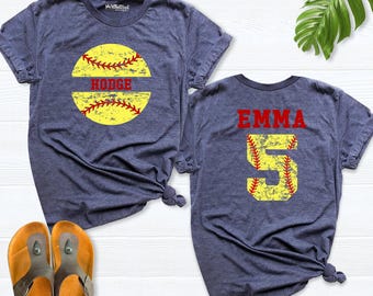 May include: Two heather navy blue t-shirts. The left shirt features a yellow softball graphic with red stitching and the name HODGE in red. The right shirt displays the name EMMA in red above a large yellow number 5 with red stitching.