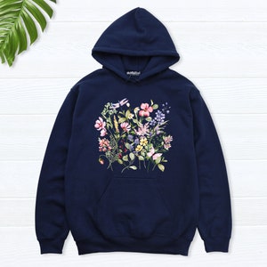 K&ouml;nnte beinhalten: Ein marineblauer Hoodie mit einem Blumendruck mit rosa, gelben, violetten und wei&szlig;en Blumen. Der Hoodie hat eine Kapuze mit Kordelzug und eine K&auml;ngurutasche.