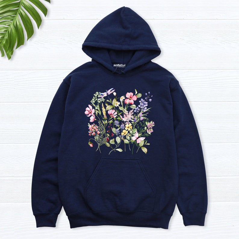 K&ouml;nnte beinhalten: Ein marineblauer Hoodie mit einem Blumendruck mit rosa, gelben, violetten und wei&szlig;en Blumen. Der Hoodie hat eine Kapuze mit Kordelzug und eine K&auml;ngurutasche.