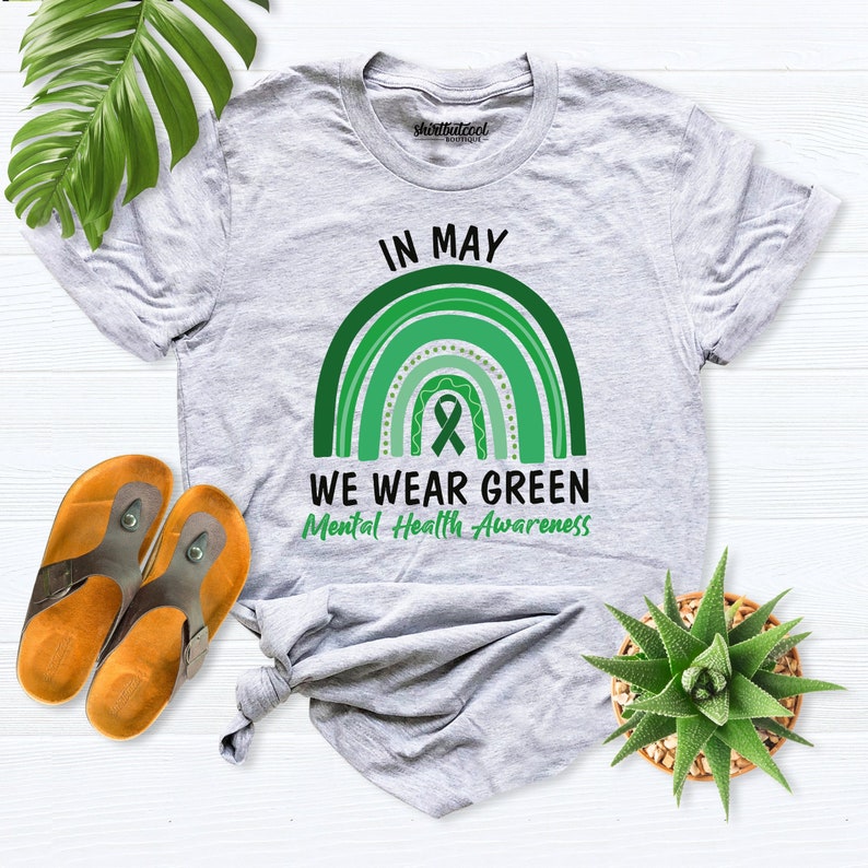 K&ouml;nnte beinhalten: Ein graues T-Shirt mit einem gr&uuml;nen Regenbogen und einem gr&uuml;nen Band. Der Text auf dem Shirt lautet "Im Mai tragen wir Gr&uuml;n f&uuml;r die psychische Gesundheit".
