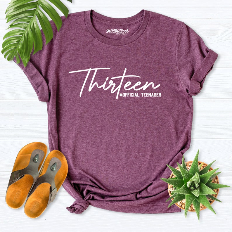 May include: A purple t-shirt with the text "Thirteen #OFFICIAL TEENAGER" in white lettering.