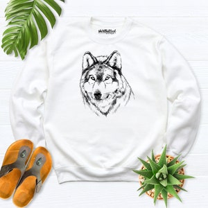 Pu&ograve; includere: Felpa bianca con un'illustrazione in bianco e nero di una testa di lupo. Il testo "shirtbutcool" &egrave; stampato sulla felpa.