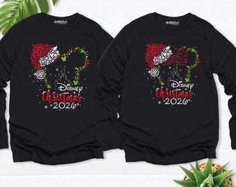 May include: Two black long-sleeve shirts featuring a graphic of a Mickey Mouse silhouette wearing a Santa hat, composed of red, green, and white dots. The design includes a castle outline, the text Disney Christmas 2026, and snowflakes.