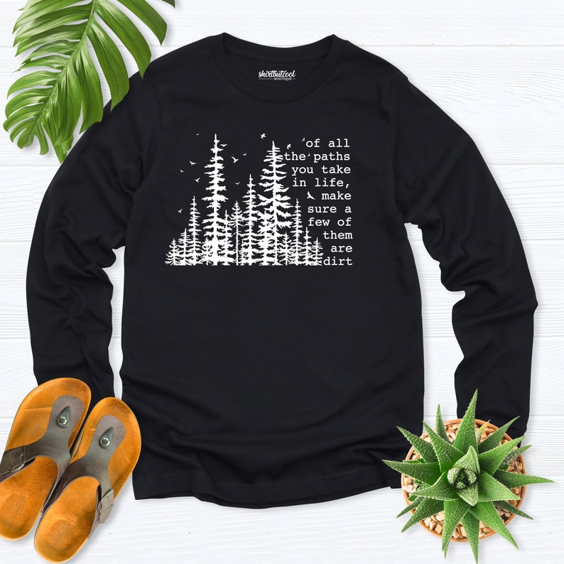 May include: Black long-sleeve shirt with a white graphic of a forest and the text "of all the' paths you take in life, make sure a few of them are dirt".