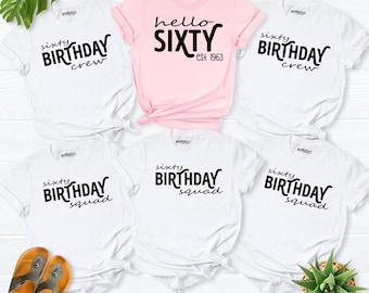 May include: A collection of five short-sleeved t-shirts featuring one light pink shirt with the text hello SIXTY est. 1963 and four white shirts with the text sixty BIRTHDAY crew or sixty BIRTHDAY squad in black lettering.