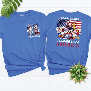 May include: Two blue t-shirts featuring Mickey and Minnie Mouse in patriotic attire. The front of the shirt displays the characters with the text "1776-2026". The back of the shirt has a design with the American flag and the words "250th YEARS ANNIVERSARY AMERICA".