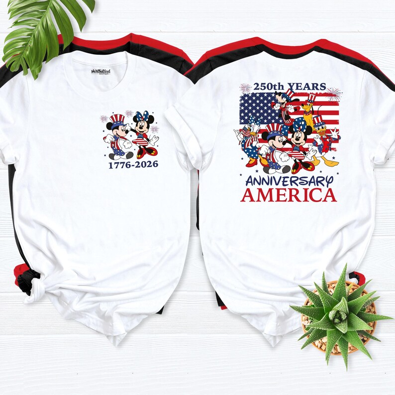 May include: Two white t-shirts with red and black trim. One shirt features Mickey and Minnie Mouse in patriotic attire with the text "1776-2026". The other shirt displays a US flag with Mickey, Minnie, and friends, and the text "250th YEARS ANNIVERSARY AMERICA".