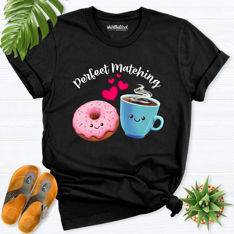 May include: Black t-shirt with the text "Perfect Matching" in white letters. A pink donut with sprinkles and a blue coffee cup with a smiley face are on the shirt.