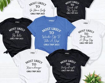 May include: A collection of seven short-sleeve t-shirts in white, black, and blue. Each shirt features the text MOST LIKELY TO followed by unique phrases like Go Home Early, Drink All The Wine, Be late, Wander Off To Take A Nap, Bring Home A Stray Dog, Kiss a stranger, or Party all night, with GIRLS TRIP 2023 printed below.