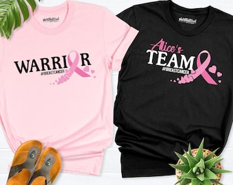 May include: A light pink t-shirt with the text WARRIOR and a pink ribbon, and a black t-shirt with the text Alice's TEAM and a pink ribbon. Both shirts feature the hashtag #BREASTCANCER and small heart graphics.