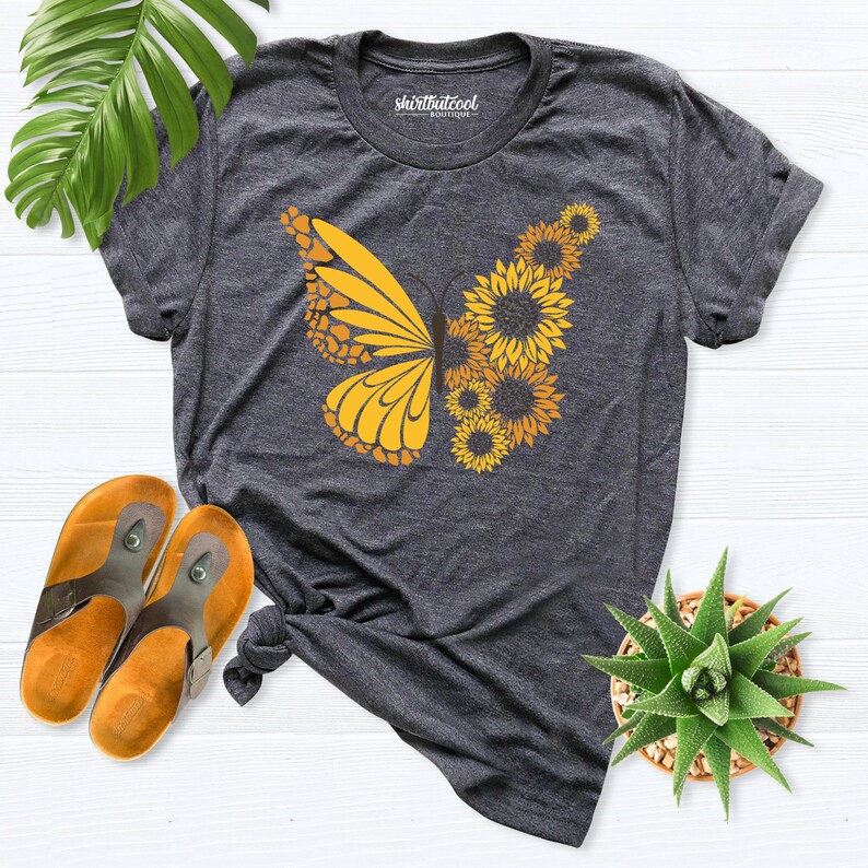 May include: A dark gray t-shirt with a yellow butterfly design made of sunflowers. The shirt has a crew neck and short sleeves.
