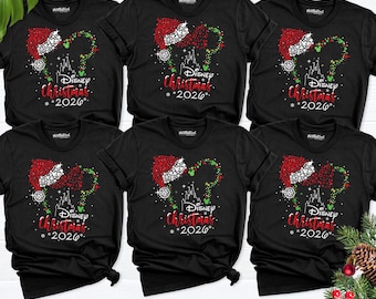 May include: Six black short-sleeve t-shirts featuring a graphic of a Santa hat and a castle silhouette. The design includes red and green dots, white sparkles, and the text Disney Christmas 2026. The shirts are arranged in two rows of three.