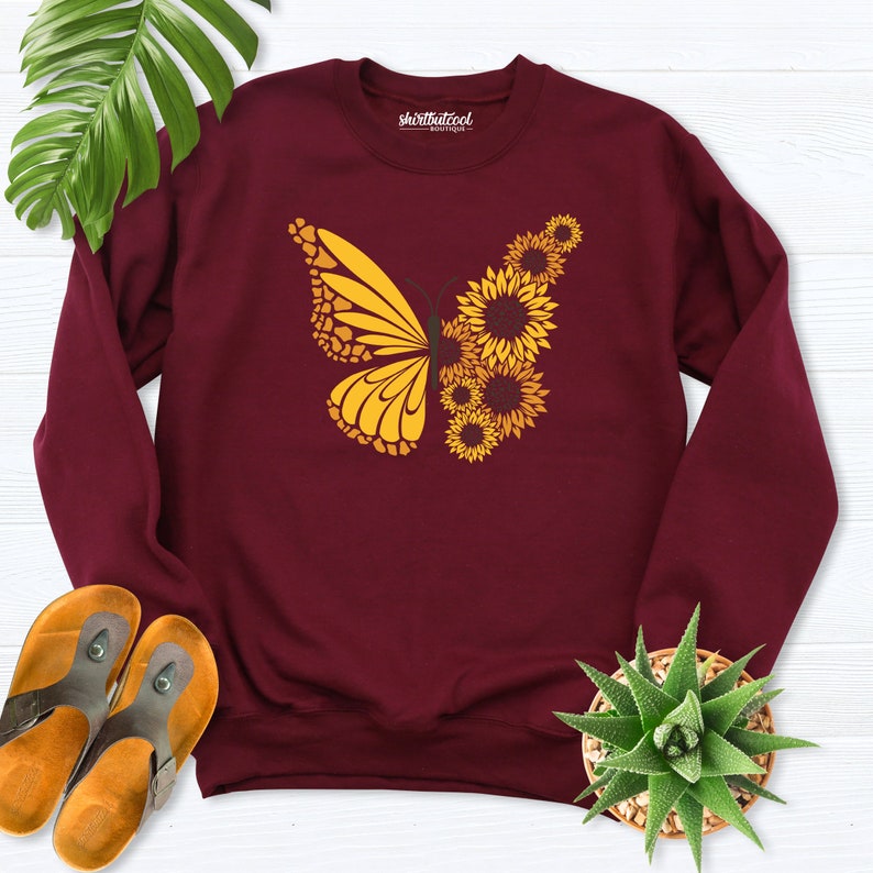 May include: Burgundy sweatshirt with a yellow butterfly design made of sunflowers. The text "shirtthatcool" is printed on the sweatshirt.