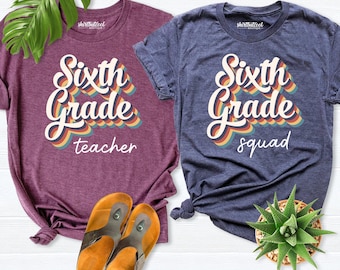 May include: A maroon t-shirt with the text Sixth Grade teacher and a navy blue t-shirt with the text Sixth Grade squad, both featuring multi-colored retro-style lettering. Two tan sandals and a green succulent plant are also visible.