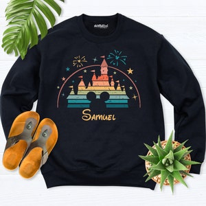 Puede incluir: Sudadera negra con una ilustraci&oacute;n de estilo retro de un castillo con fuegos artificiales y estrellas. El castillo est&aacute; en colores arco&iacute;ris con una silueta de Mickey Mouse. El nombre "Samuel" est&aacute; impreso debajo del castillo.