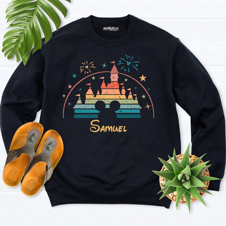 Puede incluir: Sudadera negra con una ilustraci&oacute;n de estilo retro de un castillo con fuegos artificiales y estrellas. El castillo est&aacute; en colores arco&iacute;ris con una silueta de Mickey Mouse. El nombre "Samuel" est&aacute; impreso debajo del castillo.
