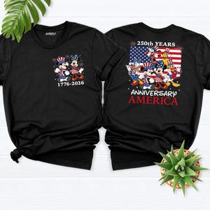 May include: Two black t-shirts featuring Mickey and Minnie Mouse in patriotic attire. One shirt displays the text "1776-2026" with the characters. The other shirt has the text "250th YEARS ANNIVERSARY AMERICA" with a flag design and multiple characters.