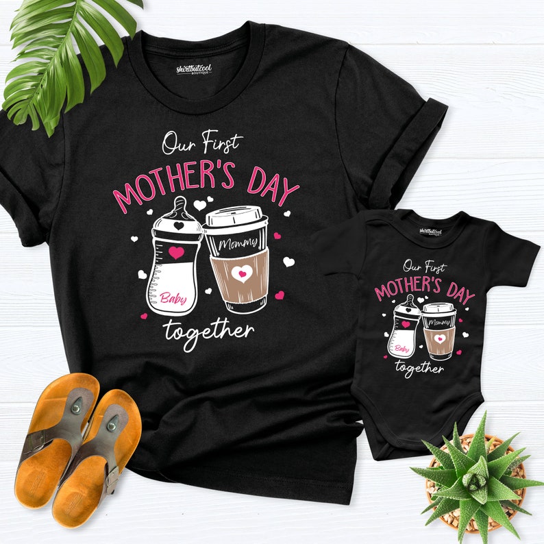 May include: Black t-shirt and onesie set with a white graphic of a baby bottle and coffee cup. The text reads "Our First Mother's Day Together".