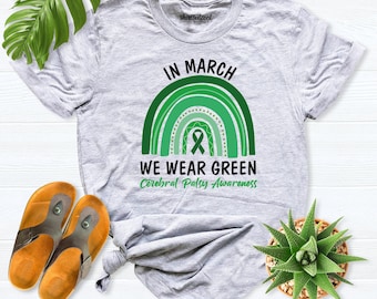 May include: A light gray short-sleeve t-shirt featuring a green rainbow graphic with the text IN MARCH WE WEAR GREEN and Cerebral Palsy Awareness. The design includes a green awareness ribbon centered within the rainbow arches.