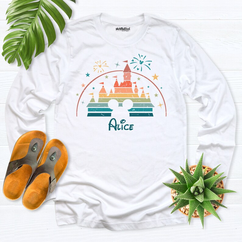Puede incluir: Camiseta blanca de manga larga con una ilustraci&oacute;n retro de un castillo con fuegos artificiales y el nombre "Alice" impreso debajo.