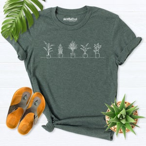 Puede incluir: Una camiseta verde oscuro con un contorno blanco de seis plantas en maceta. El texto "shirtbutcool boutique" est&aacute; impreso en la camiseta.