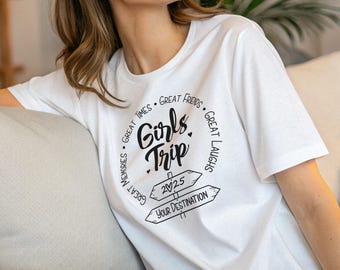 May include: A white short-sleeved t-shirt featuring black text that reads Girls Trip in the center, surrounded by a circular border of words including Great Times, Great Friends, Great Laughs, and Great Memories, with 2025 on a sign.