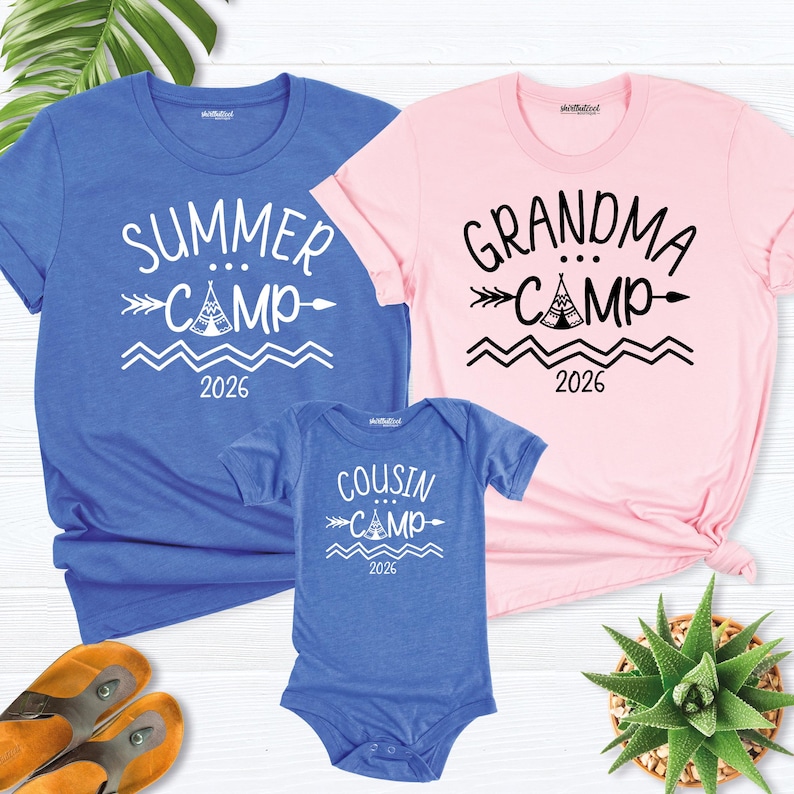 May include: A blue t-shirt with "Summer Camp 2026" text, a pink t-shirt with "Grandma Camp 2026" text, and a blue onesie with "Cousin Camp 2026" text. The text is in white. The shirts and onesie are short-sleeved.