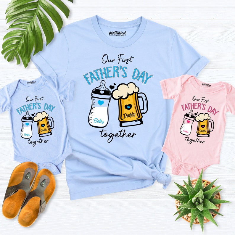May include: A set of three light blue and pink t-shirts with the text "Our First Father's Day together" and a graphic of a baby bottle and a beer mug. The baby bottle is labeled "Baby" and the beer mug is labeled "Daddy".