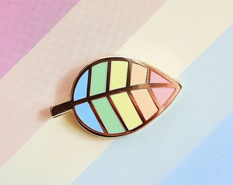 Puede incluir: Un pin de esmalte de hoja arcoíris en una tarjeta blanca con el texto "misomomo" y el nombre de usuario de las redes sociales "@misomomo_" y el sitio web "misomomo.com".