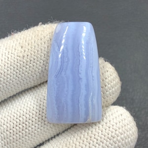 Könnte beinhalten: Ein hellblauer Achat-Cabochon mit weißen Bändern. Der Cabochon ist glatt und poliert und hat eine leicht längliche Form.