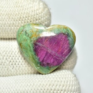 Peut inclure: Une pierre précieuse en forme de cœur avec un centre magenta vif et une couche extérieure verte et dorée. La pierre polie est présentée sur un fond blanc, mettant en valeur ses couleurs et textures naturelles. Parfait pour la joaillerie ou comme objet décoratif.