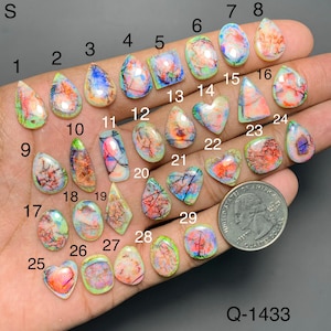 May include: A collection of twenty-nine polished, multi-colored cabochon gemstones with iridescent patterns, numbered 1 through 29, displayed alongside a United States quarter coin for scale. Each stone features unique swirls of pink, blue, and green.