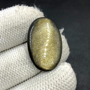 Obsidiaan cabochon goudglans... Ovale cabochon... 28 x 18 x 4 mm... 15 kts... A#N5446