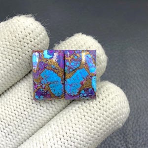 May include: Two rectangular gemstones with a vibrant pattern of turquoise, purple, and gold. The stones have a polished surface and are set against a neutral background. The gemstones are likely for jewelry making.