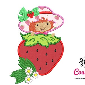 Könnte beinhalten: Stickerei mit einer Erdbeere und einem Mädchen, das einen rosa Hut trägt und eine Blume hält. Die Erdbeere ist rot mit grünen Blättern und schwarzen Samen. Das Mädchen hat rote Haare und ein rosa Kleid.