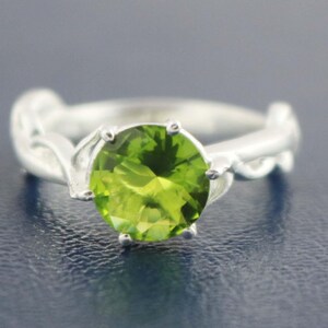 May include: A silver ring with a green gemstone set in a leaf-like design.